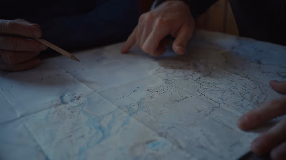 Two hands pointing and marking locations on a folded paper map.