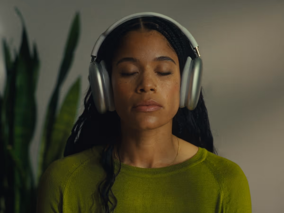 Calm woman with closed eyes wearing silver over-ear headphones and a green sweater.