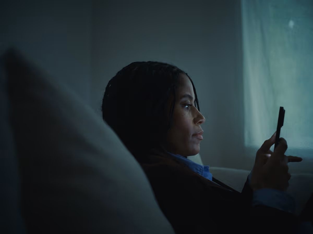 Woman sitting in dim light looking at her smartphone.