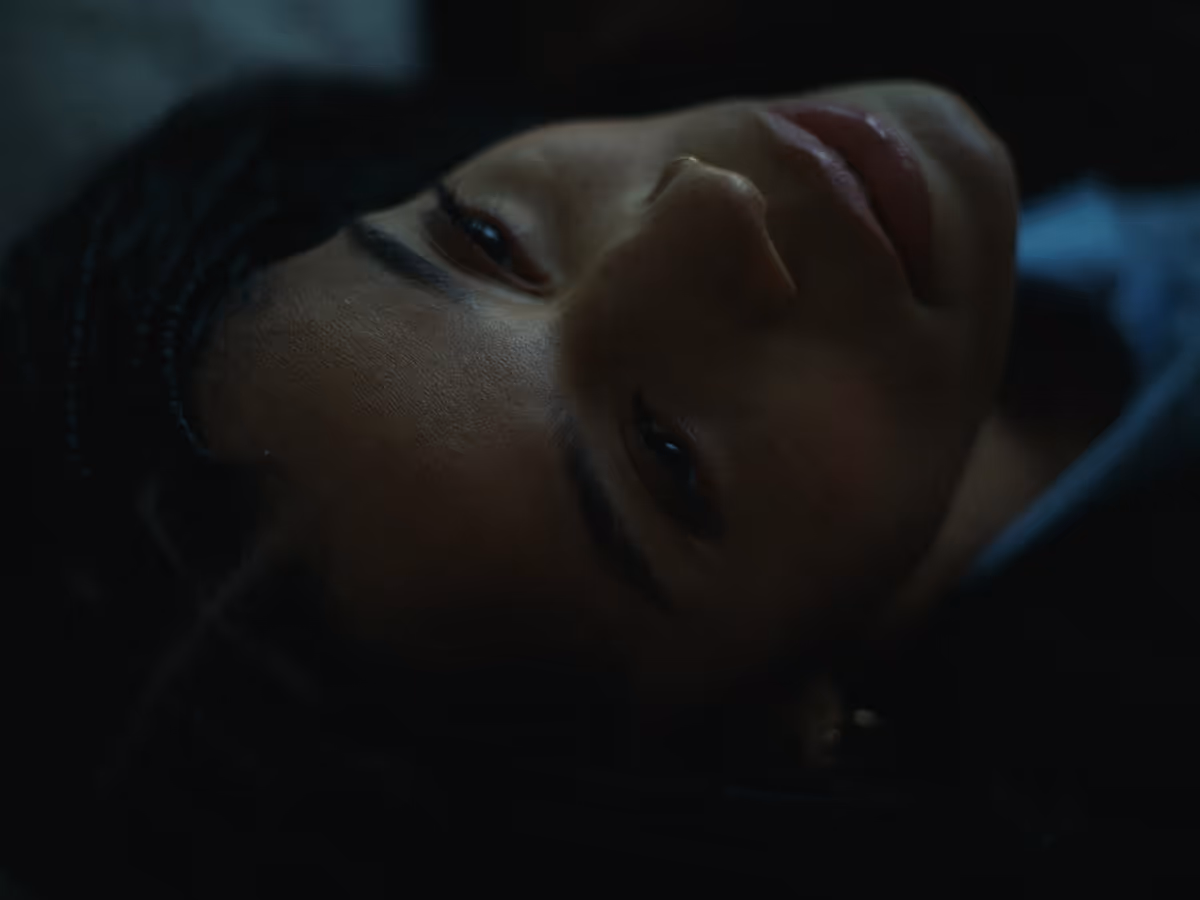 Close-up of a woman's face lying sideways in dim lighting with a contemplative expression.