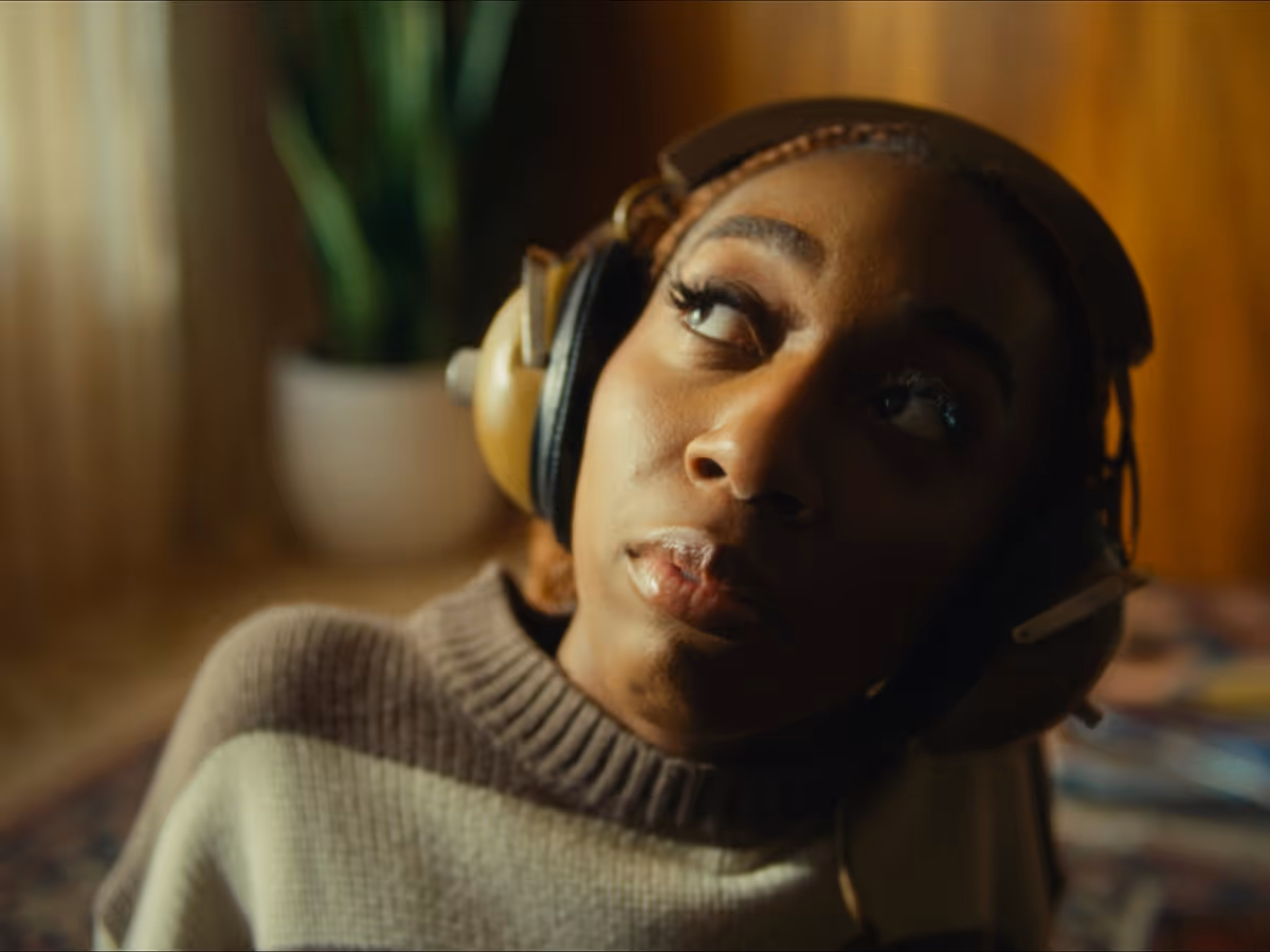 Woman wearing large headphones and a striped sweater looking thoughtfully to the side indoors.