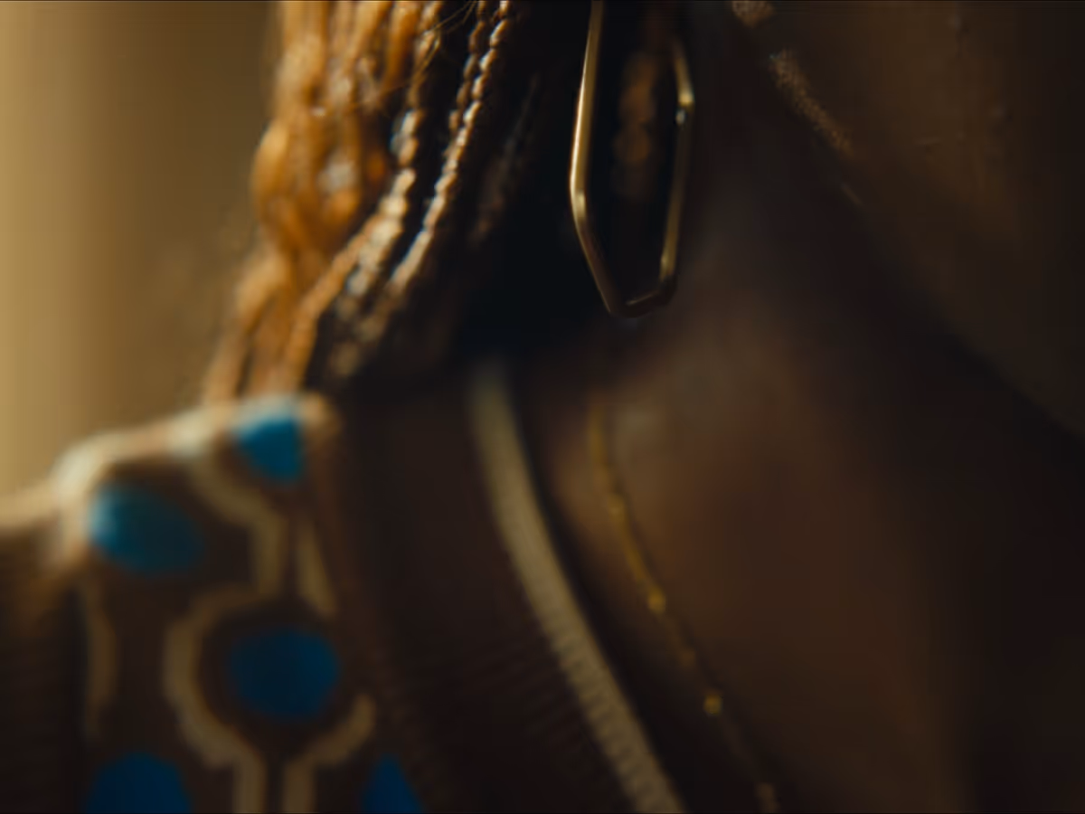 Close-up of a person with braided hair and a gold hoop earring wearing a colorful patterned garment.