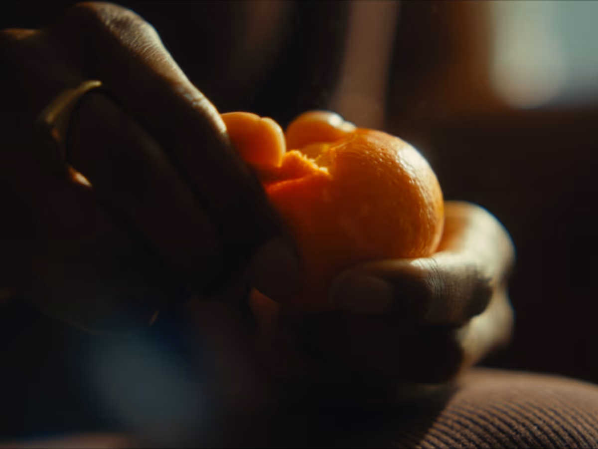 Close-up of hands peeling an orange in warm, low light.