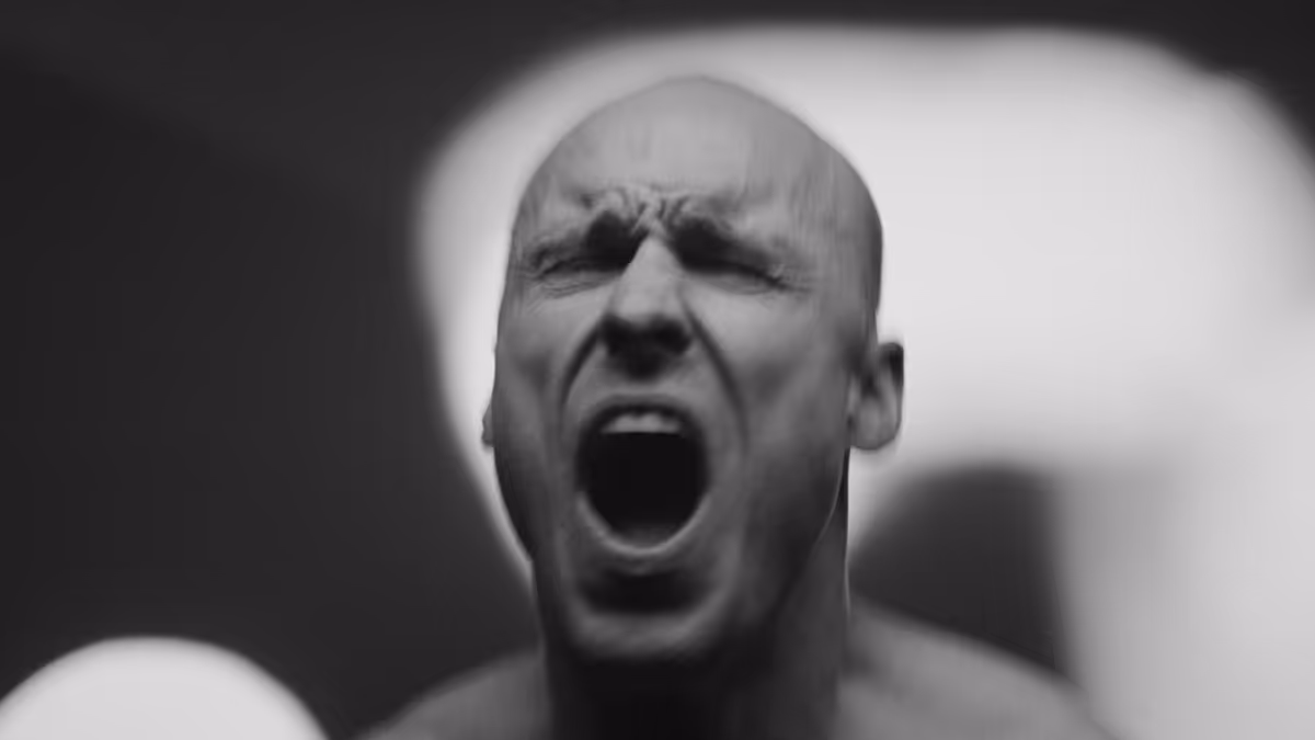 Black and white close-up of a bald man with eyes closed and mouth wide open, appearing to shout or scream.