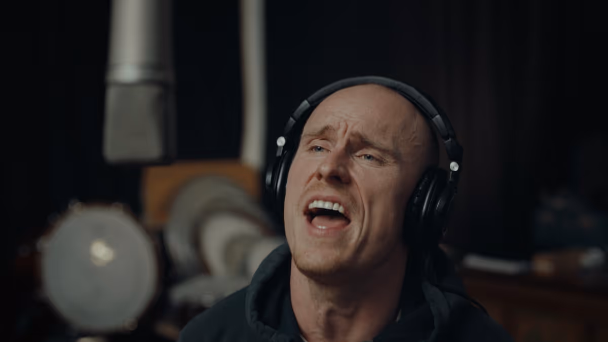 Man wearing headphones singing passionately in a recording studio with a microphone visible in the background.