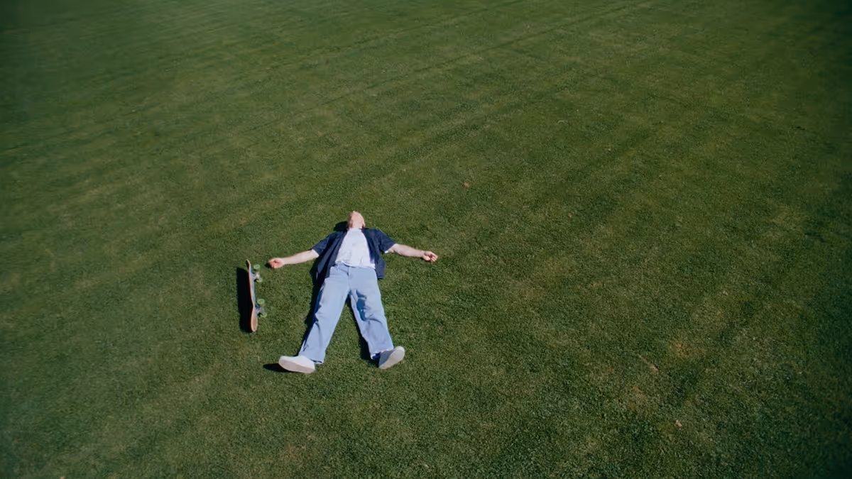 Person lying on their back on green grass with a skateboard beside them.
