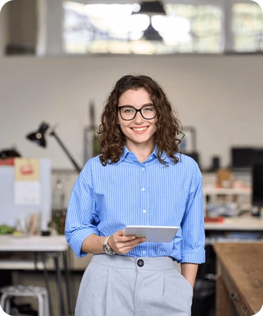 Smiling woman holding a digital tablet while standing in a modern office workspace.
