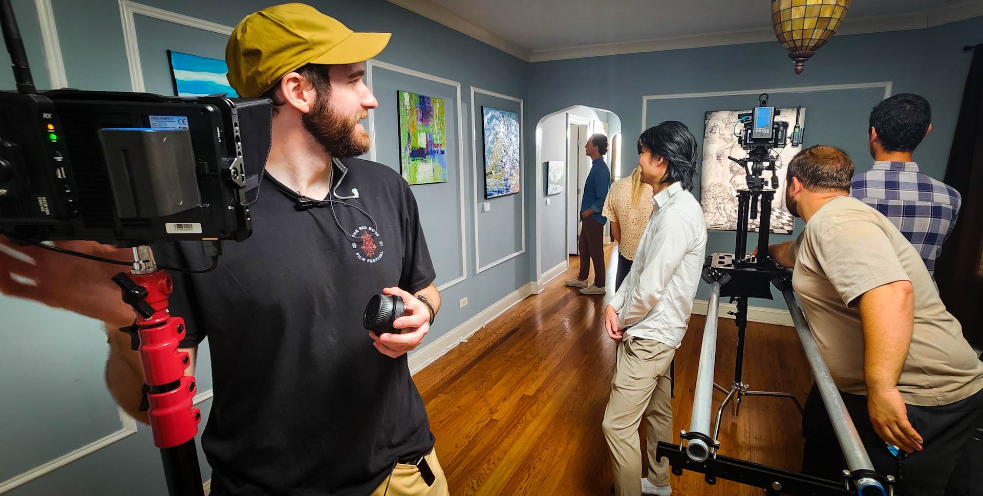 Film crew operating a camera on a dolly track filming inside an art gallery with paintings on blue walls.
