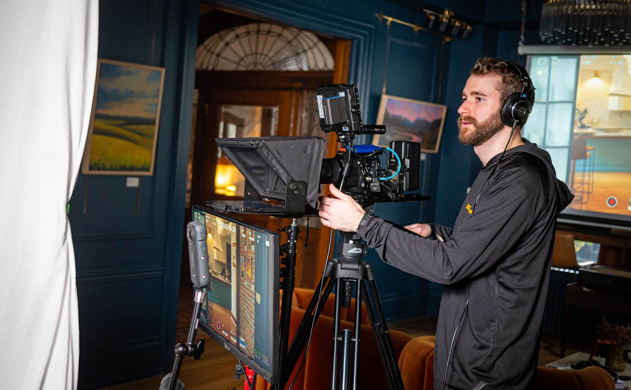 Man wearing headphones operating a professional video camera mounted on a tripod indoors.