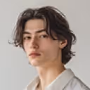 Young man with medium-length dark hair wearing a light-colored shirt against a plain background.