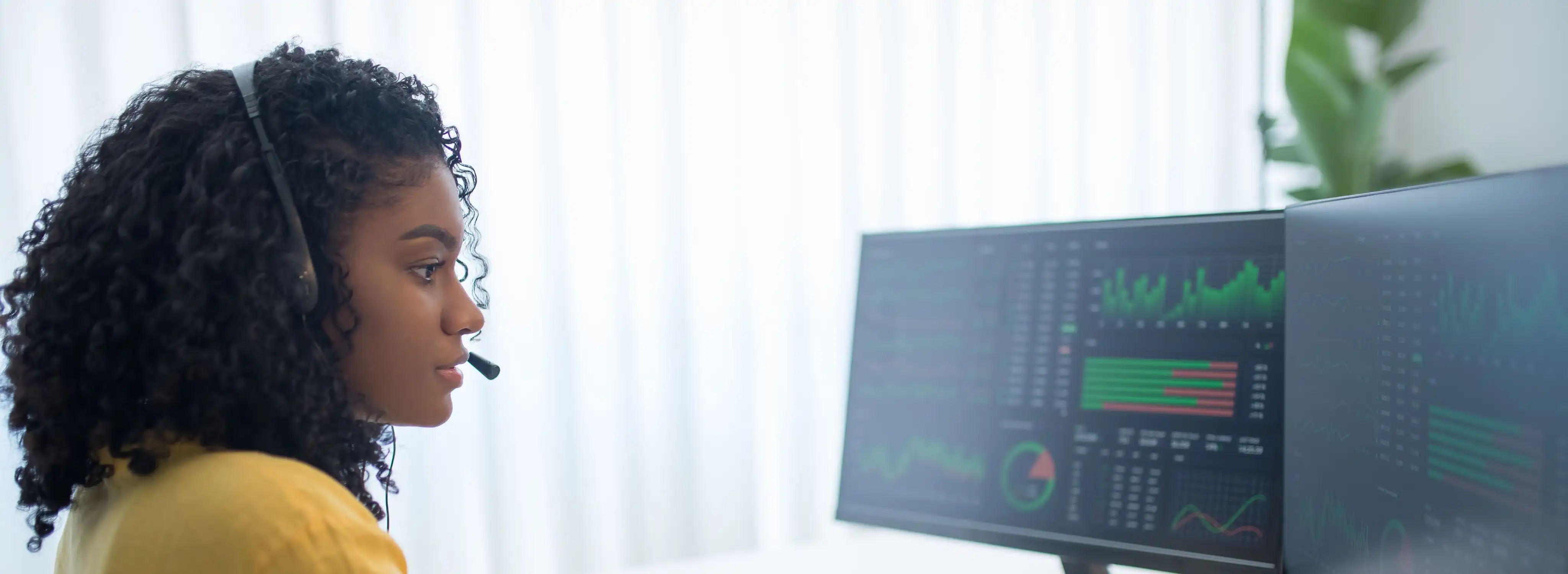 A woman wearing a headset works at a computer with multiple monitors.