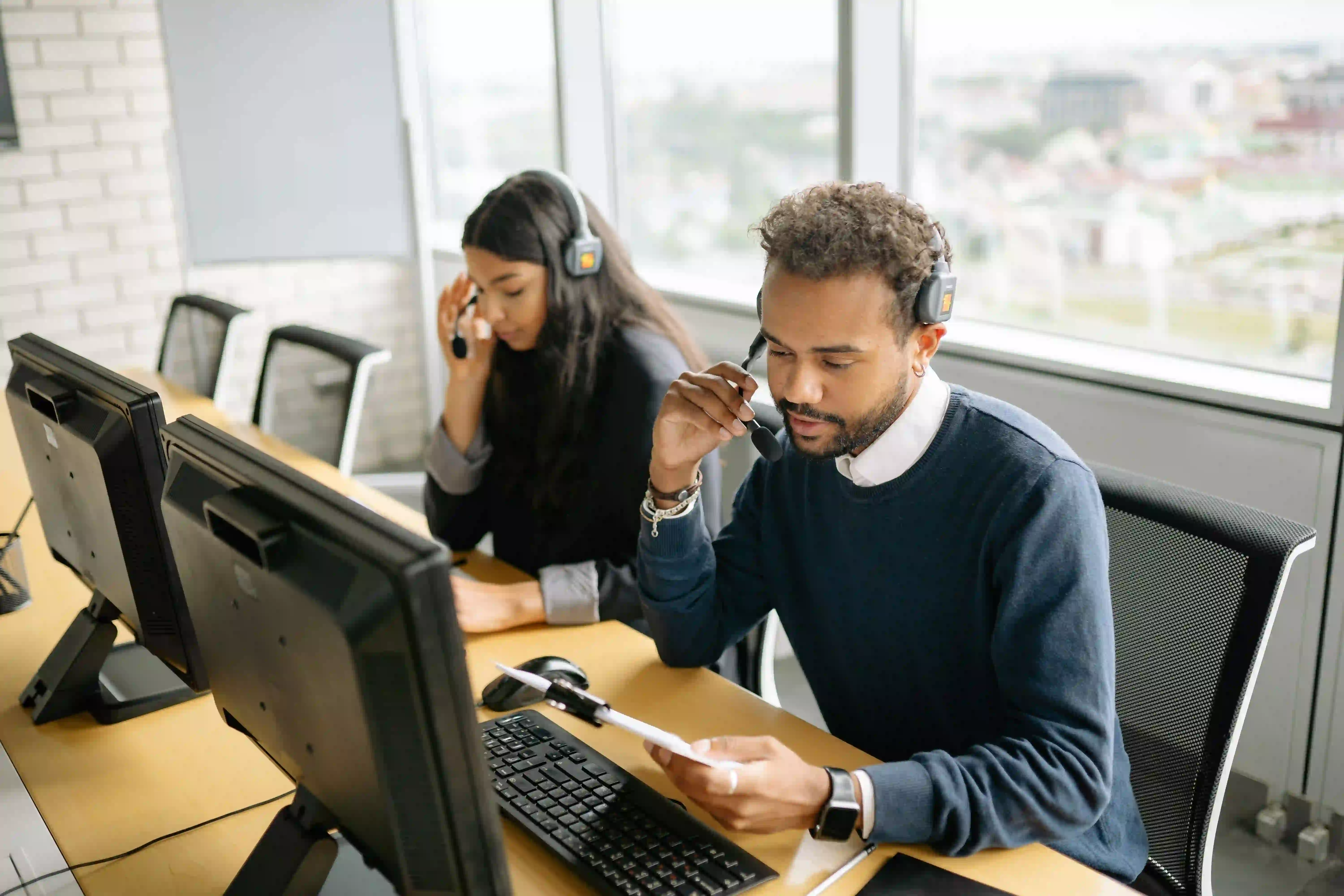 Two customer service representatives wearing headsets work at computers in a contact center.