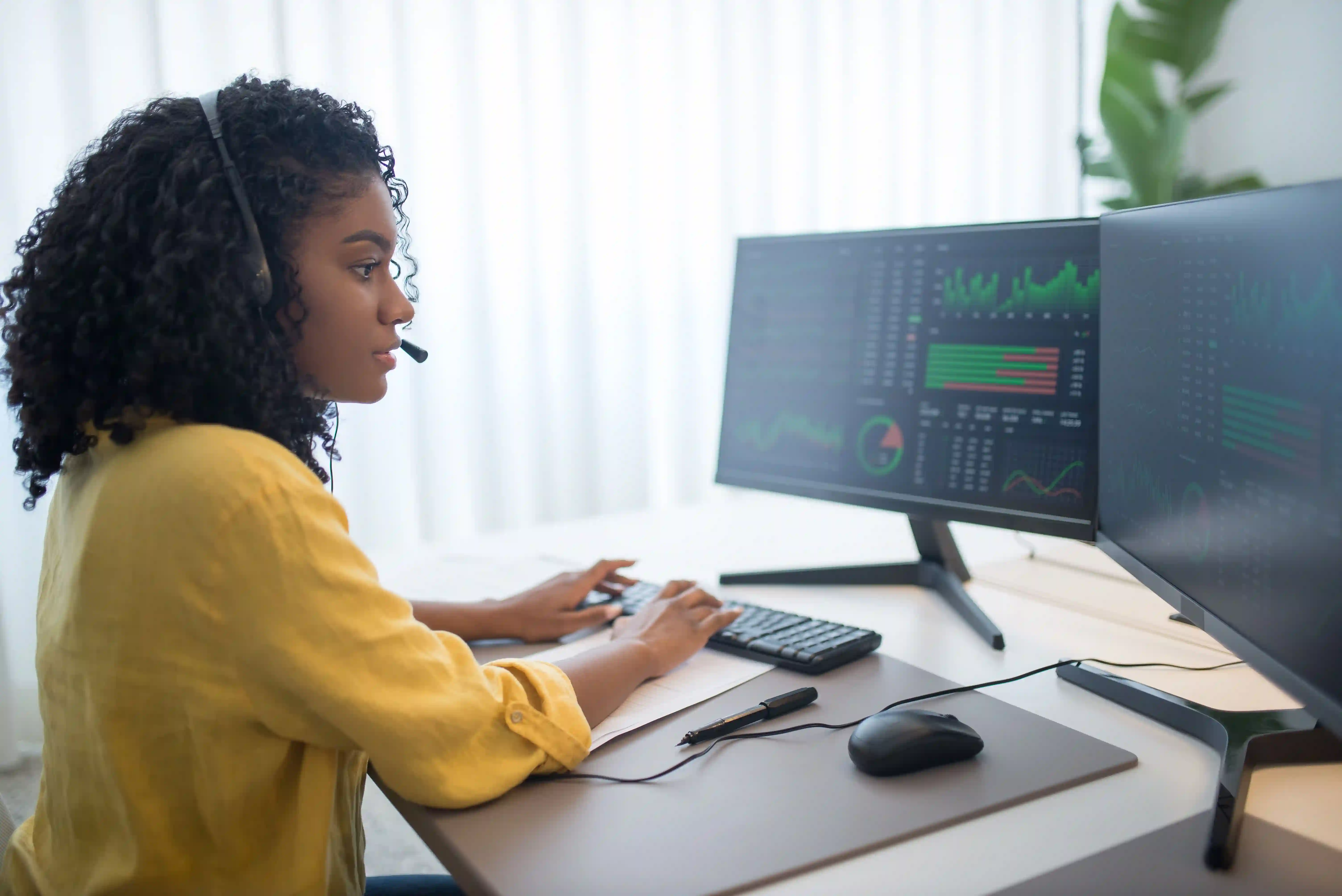 A woman wearing a headset works at a computer with multiple monitors.