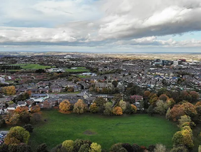 Aerial view over Barnsley showing rooftops, autumn trees and a green park under a cloudy sky