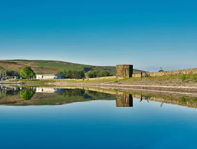 Still reservoir near Blackburn reflecting a stone tower, grassy hillside and clear blue sky