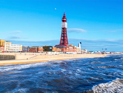 Blackpool Tower rising above the promenade and beach, with waves rolling in under a blue sky