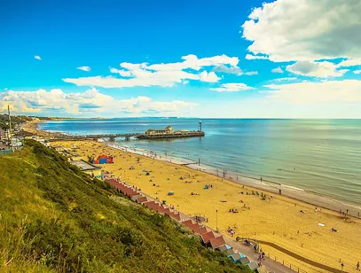Golden sandy beach and pier at Bournemouth, with beach huts and a grassy cliff in the foreground