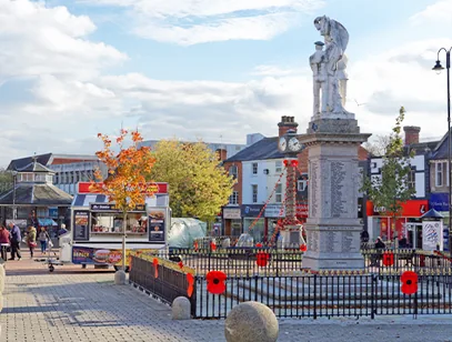 War memorial with a stone statue on a town square in Cannock, with poppies on the railings and a market stall