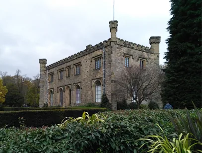 Battlemented stone hall with tall windows set behind hedges and trees in Burnley