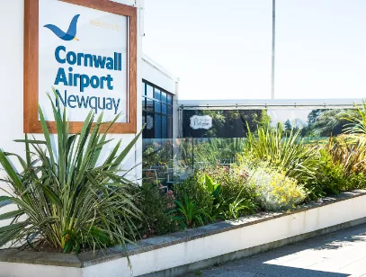 Cornwall Airport Newquay sign on the terminal wall above a planted border of palms and shrubs