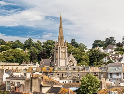 Church spire rising above tiled rooftops and trees in a hillside town