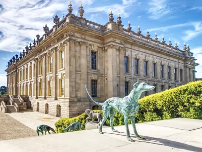 Grand stately home with a classical facade and bronze greyhound sculptures in the Derbyshire countryside