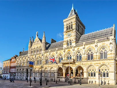 Ornate Gothic Revival town hall with a clock tower on a sunny square in Northamptonshire