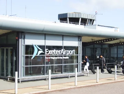 Exeter Airport terminal entrance with travellers walking past the glass frontage and control tower