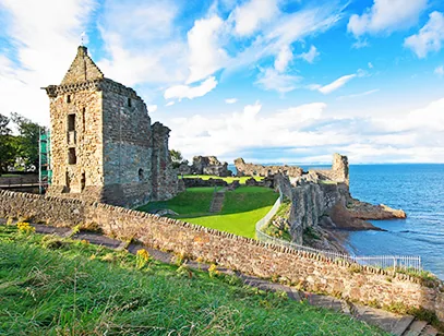 Ruined coastal castle and stone walls above a green lawn and blue sea in Fife