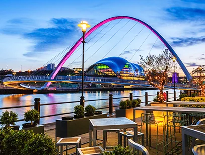 Gateshead Millennium Bridge lit pink at dusk over the Tyne, with the Sage building and a riverside terrace