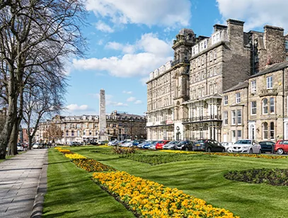 Yellow flower beds and a stone obelisk beside grand Victorian buildings on a sunny day in Harrogate