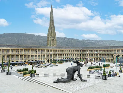 Piece Hall courtyard in Halifax with a bronze sculpture in the foreground and a church spire behind