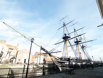 Tall-masted historic sailing warship moored in a dock beside old brick buildings in Hartlepool