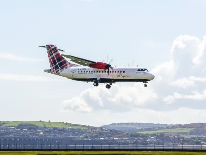 Turboprop plane in tartan-tailed livery coming in to land over green hills in the Highlands and Islands