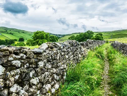 Drystone wall and grassy footpath leading into rolling green Yorkshire Dales countryside near Keighley