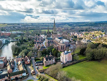 Aerial view of Lichfield Cathedral's spires above surrounding houses and a pool
