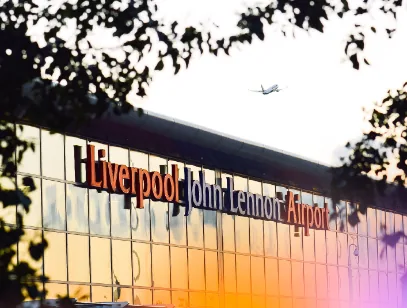 Liverpool John Lennon Airport terminal sign glowing at sunset with a plane in the sky