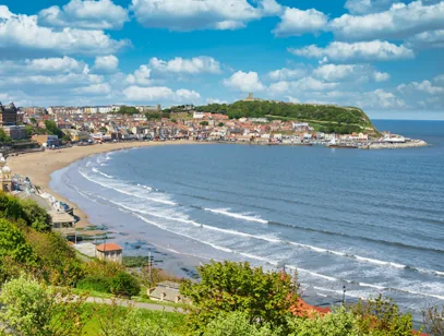 Curved sandy bay and seafront town beneath a wooded headland on the North Yorkshire coast
