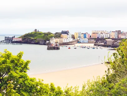 Colourful harbourside houses above a sandy beach and boats on the Welsh coast