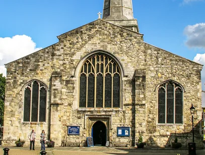 Medieval stone church with a large arched window and people at the entrance in Loughborough