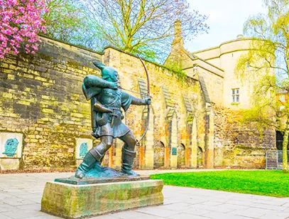 Robin Hood statue drawing his bow beside old sandstone castle walls in Nottinghamshire