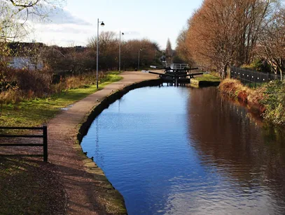 Canal lock and towpath running beside still water lined with autumn trees in Rochdale