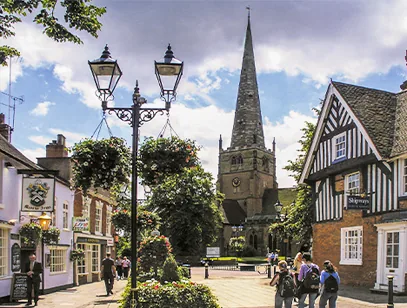 Church spire rising above a village street with hanging baskets and a timber-framed building in Solihull