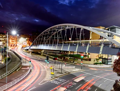 Arched footbridge above a busy road with light trails at night in Sheffield