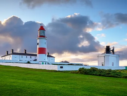 Red and white striped lighthouse on a grassy clifftop under a cloudy sky in South Tyneside
