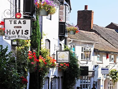 Flower-decked tea rooms and cottages with hanging signs on a sunny street in Stafford