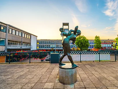 Bronze sculpture of a mother and child on a paved square with shops behind in Stevenage