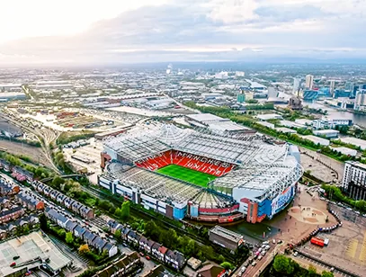 Aerial view of Old Trafford stadium with terraced streets and the Manchester skyline beyond