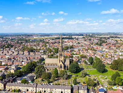 Aerial view of a stone church with a tall spire amid rows of terraced houses in Wakefield