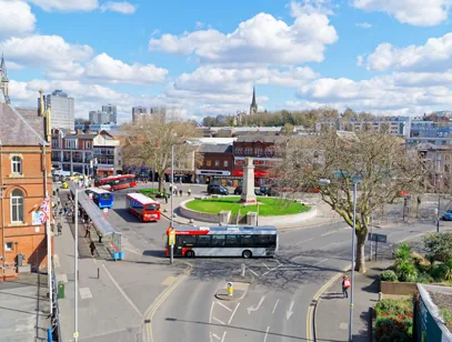 Town centre roundabout with a monument, buses and shopfronts under a blue sky in Walsall